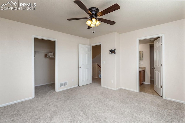 unfurnished bedroom with light carpet, ensuite bathroom, ceiling fan, a spacious closet, and a closet