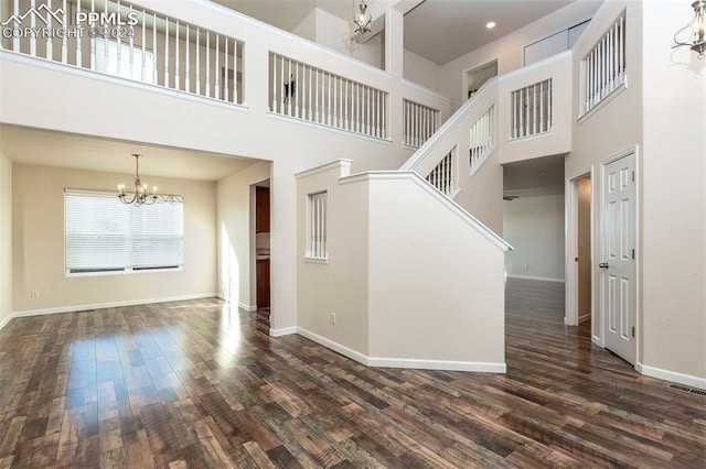 unfurnished living room with dark hardwood / wood-style floors, a towering ceiling, and a chandelier