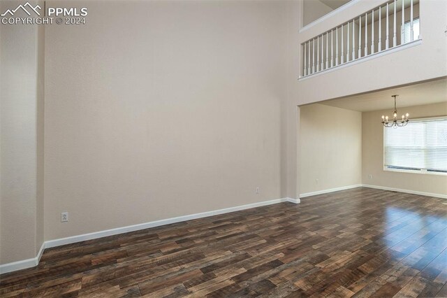 spare room with dark wood-type flooring, a high ceiling, and a chandelier