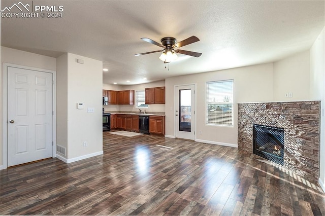 unfurnished living room with dark hardwood / wood-style flooring, a textured ceiling, ceiling fan, sink, and a stone fireplace