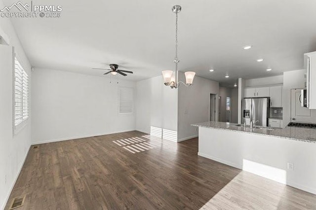 kitchen with stainless steel fridge with ice dispenser, ceiling fan with notable chandelier, white cabinets, and light stone counters