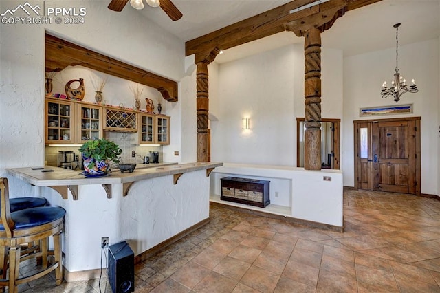 kitchen with kitchen peninsula, decorative columns, ceiling fan with notable chandelier, decorative light fixtures, and a breakfast bar area