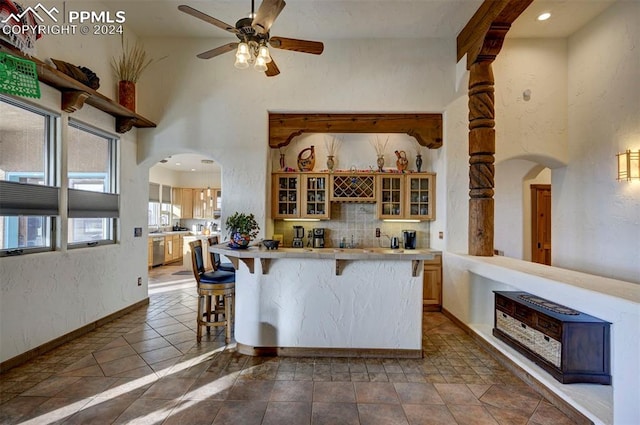 kitchen featuring tile countertops, stainless steel dishwasher, ceiling fan, decorative backsplash, and a kitchen bar