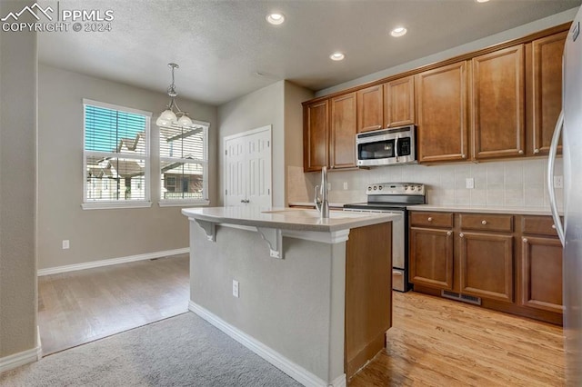 kitchen with light hardwood / wood-style flooring, pendant lighting, a center island with sink, and appliances with stainless steel finishes