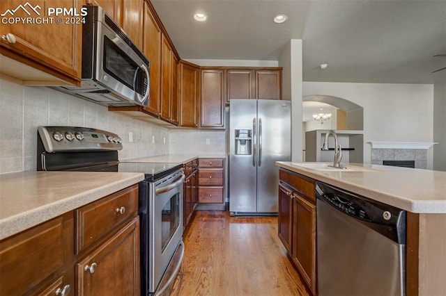 kitchen with sink, decorative backsplash, a fireplace, light hardwood / wood-style floors, and stainless steel appliances