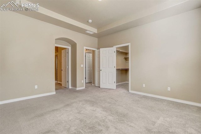 unfurnished bedroom featuring a walk in closet, light colored carpet, and a closet