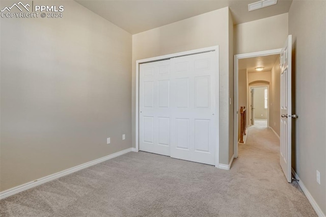 unfurnished bedroom with light colored carpet and a closet