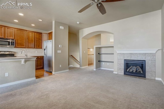 kitchen featuring stainless steel appliances, ceiling fan, sink, a breakfast bar area, and a tiled fireplace