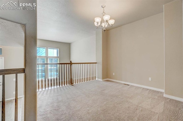 carpeted spare room featuring a notable chandelier and a textured ceiling