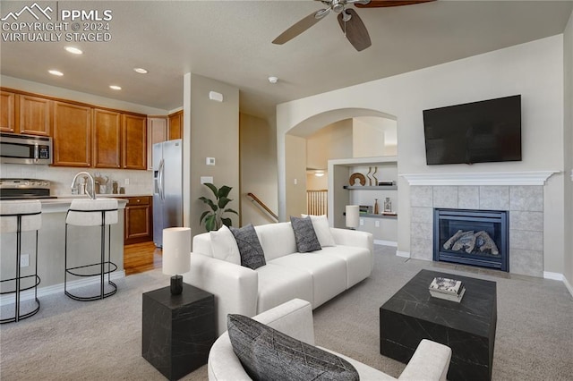 carpeted living room with a fireplace, ceiling fan, and sink