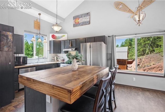 kitchen with pendant lighting, sink, high vaulted ceiling, stainless steel appliances, and a kitchen island