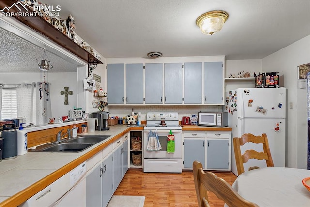 kitchen featuring white appliances, sink, light hardwood / wood-style flooring, a textured ceiling, and tile counters