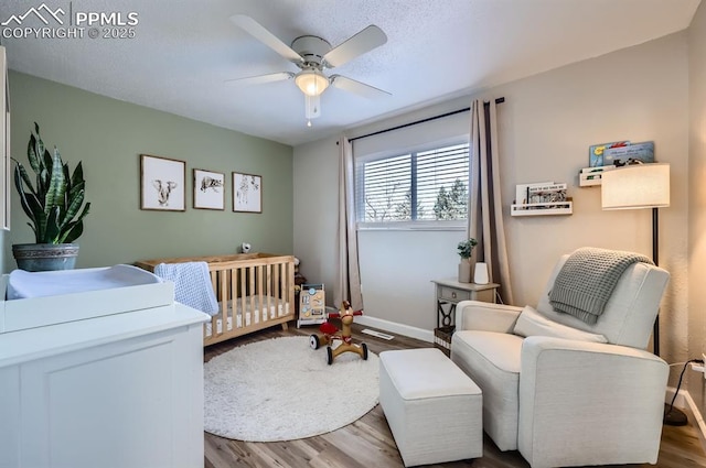 bedroom with a nursery area, dark hardwood / wood-style floors, and ceiling fan