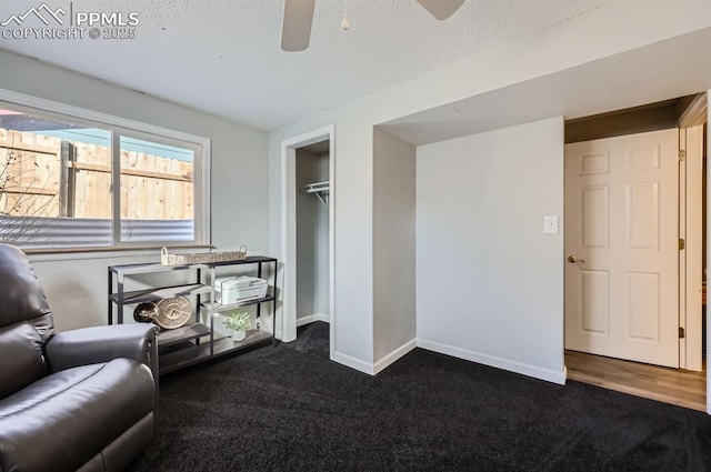 living area featuring ceiling fan, dark carpet, and a textured ceiling