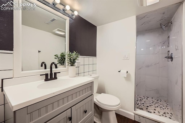 bathroom featuring tile walls, hardwood / wood-style floors, a tile shower, vanity, and toilet