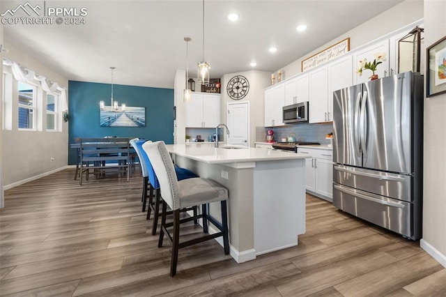 kitchen featuring sink, stainless steel appliances, decorative light fixtures, a kitchen island with sink, and white cabinets