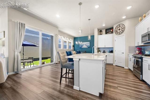 kitchen featuring stainless steel appliances, sink, white cabinetry, hanging light fixtures, and an island with sink