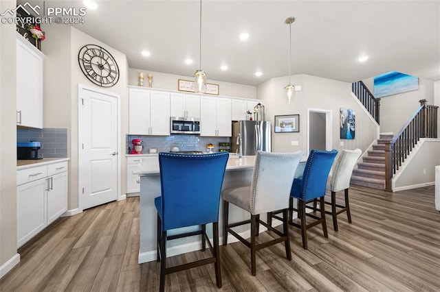 kitchen with a center island with sink, white cabinets, hanging light fixtures, and appliances with stainless steel finishes