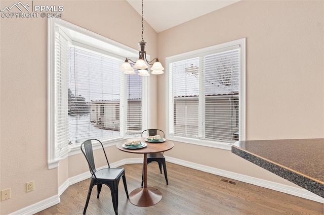 dining space featuring hardwood / wood-style floors, vaulted ceiling, a wealth of natural light, and a notable chandelier