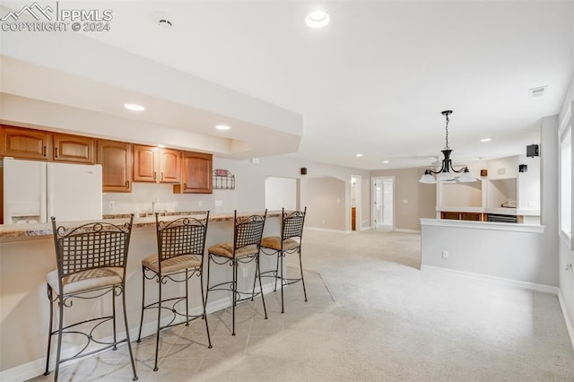 kitchen featuring light stone countertops, light carpet, a kitchen breakfast bar, pendant lighting, and white fridge with ice dispenser