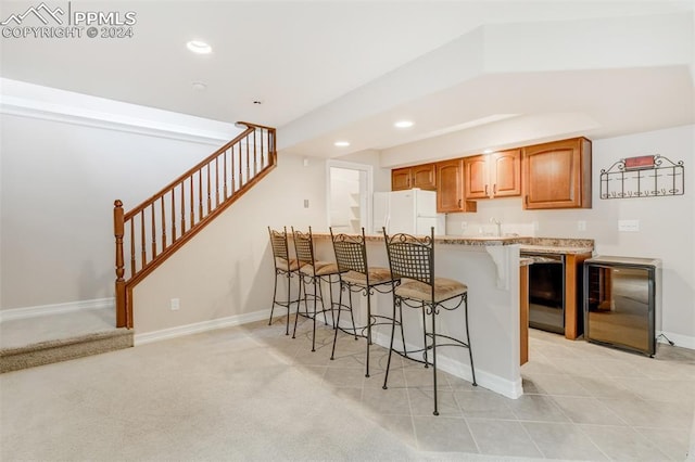 kitchen featuring a kitchen bar, wine cooler, white fridge, and light colored carpet