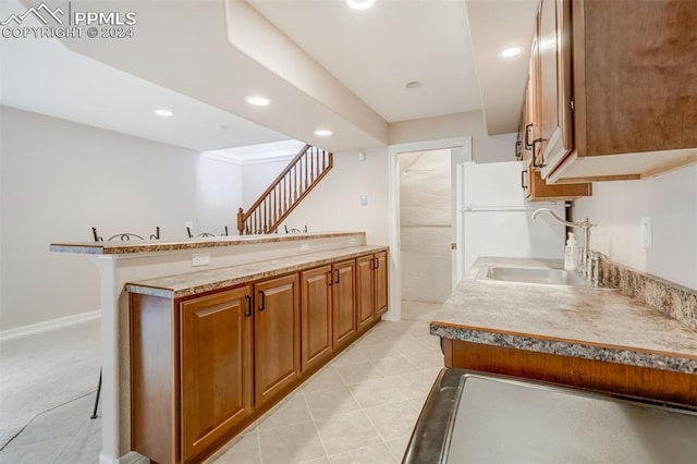 kitchen with kitchen peninsula, a breakfast bar, light tile patterned floors, and sink