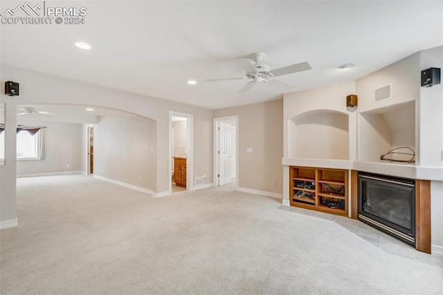 unfurnished living room with light carpet, ceiling fan, and a tiled fireplace