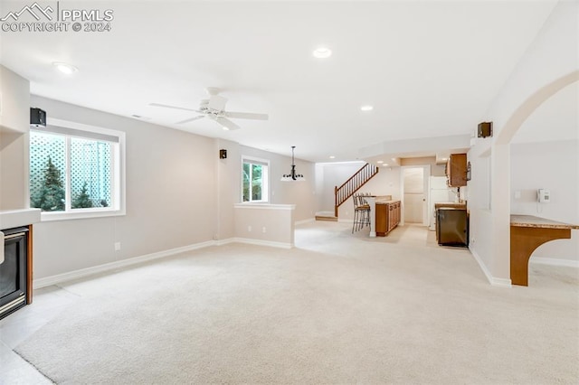 unfurnished living room with light carpet, plenty of natural light, and ceiling fan with notable chandelier