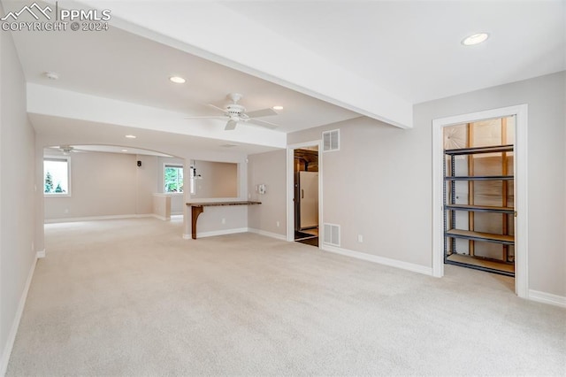 unfurnished living room featuring beamed ceiling, ceiling fan, and light carpet