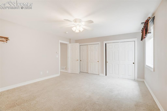 unfurnished bedroom with ceiling fan, light colored carpet, and multiple closets