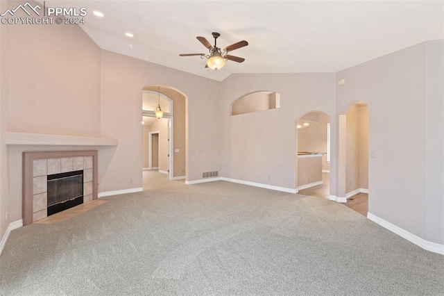 unfurnished living room featuring a tiled fireplace, ceiling fan, light carpet, and vaulted ceiling