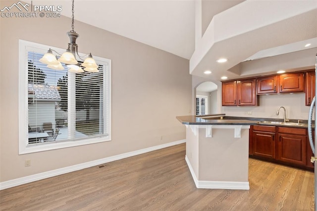 kitchen with sink, decorative light fixtures, light hardwood / wood-style flooring, a notable chandelier, and a kitchen bar