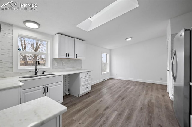 kitchen with stainless steel refrigerator, white cabinetry, sink, a healthy amount of sunlight, and backsplash