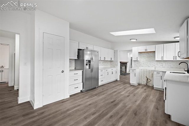 kitchen featuring white cabinets, sink, stainless steel refrigerator with ice dispenser, vaulted ceiling with skylight, and tasteful backsplash