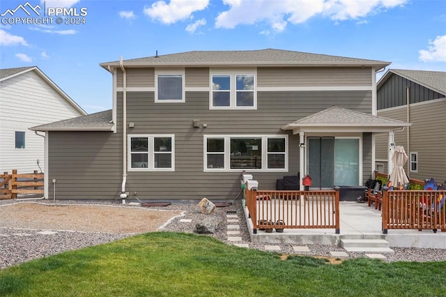 back of house with a lawn, a wooden deck, and a patio