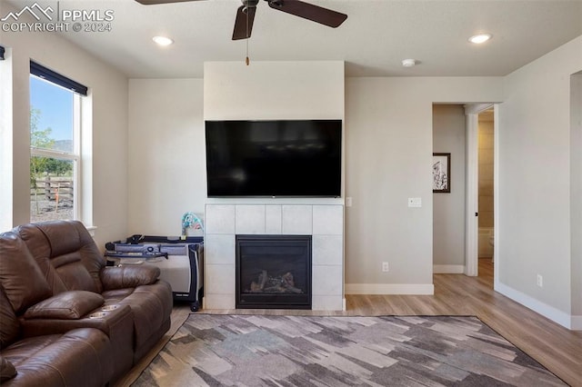 living room with wood-type flooring, ceiling fan, and a tiled fireplace