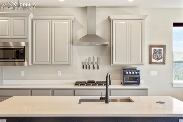 kitchen featuring appliances with stainless steel finishes, sink, a center island with sink, and wall chimney range hood