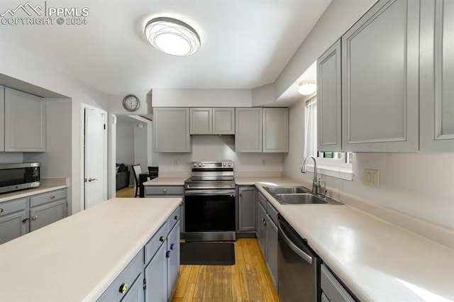 kitchen featuring appliances with stainless steel finishes, light wood-type flooring, gray cabinets, and sink