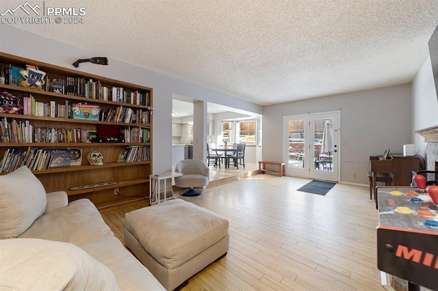 living room with a fireplace, french doors, a textured ceiling, and light hardwood / wood-style flooring