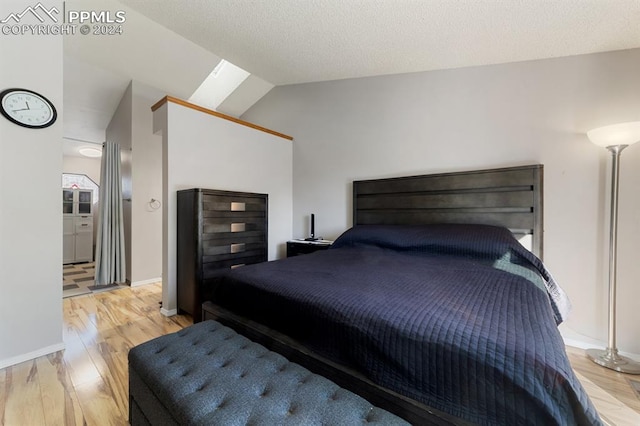 bedroom featuring vaulted ceiling with skylight, a textured ceiling, and light wood-type flooring