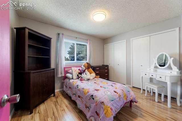 bedroom with a textured ceiling, two closets, and light hardwood / wood-style flooring