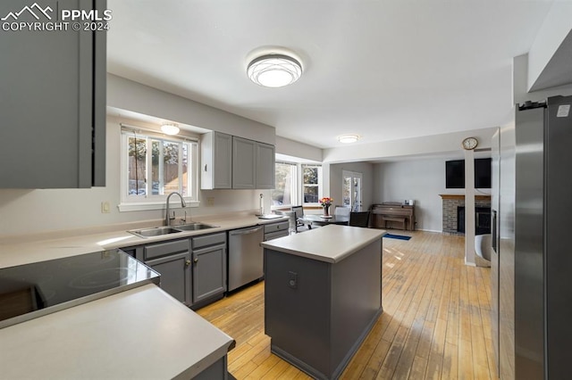 kitchen with sink, a brick fireplace, light hardwood / wood-style floors, a kitchen island, and appliances with stainless steel finishes