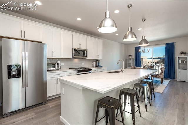 kitchen featuring a kitchen island with sink, white cabinets, hanging light fixtures, sink, and appliances with stainless steel finishes