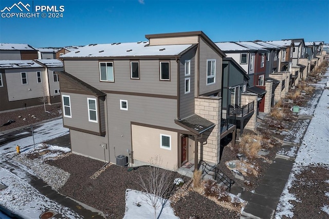 snow covered rear of property featuring central AC