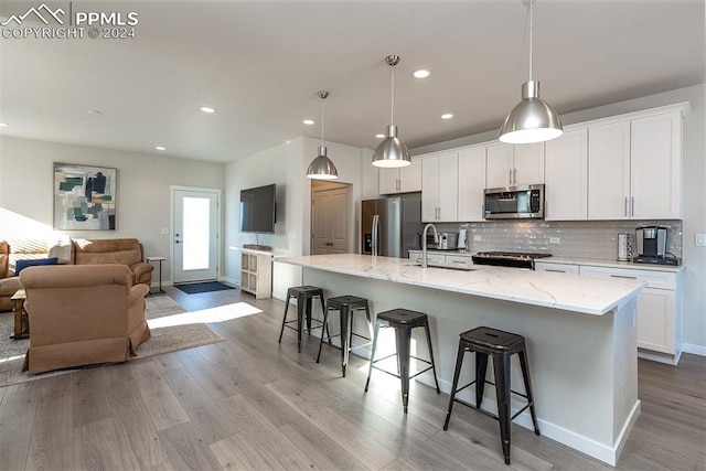 kitchen featuring light wood-type flooring, stainless steel appliances, a spacious island, white cabinets, and hanging light fixtures