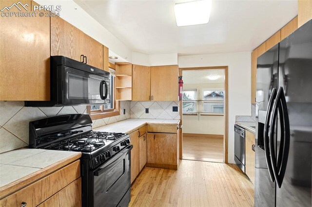 928 Alexander Rd, Colorado Springs, CO 80909 - kitchen with black appliances, decorative backsplash, light hardwood / wood-style floors, and tile countertops