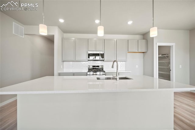 kitchen featuring a large island with sink, sink, light wood-type flooring, decorative light fixtures, and stainless steel appliances