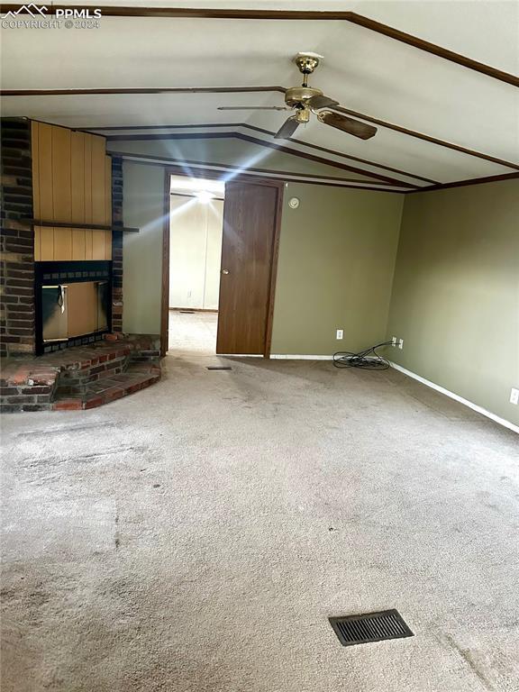 unfurnished living room featuring carpet flooring, a brick fireplace, and lofted ceiling