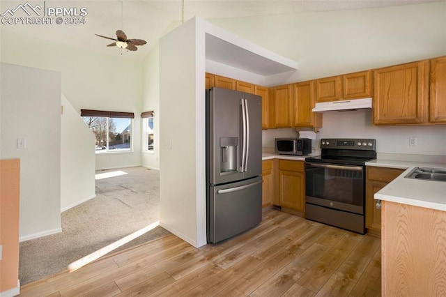 kitchen with a towering ceiling, stainless steel appliances, ceiling fan, sink, and light hardwood / wood-style floors