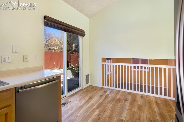 kitchen featuring a textured ceiling, light hardwood / wood-style flooring, stainless steel dishwasher, and lofted ceiling